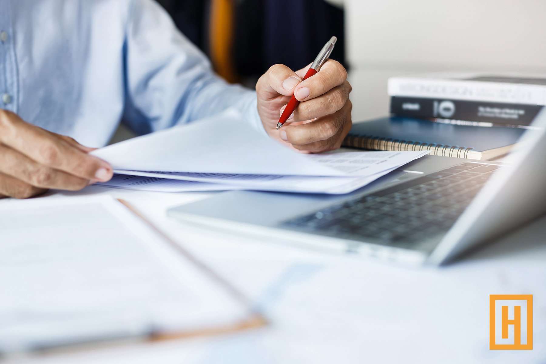 person in suit using a pen in front of a laptop
